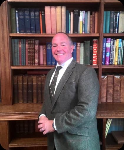 Dr John McKerrow, standing before a wall of history books